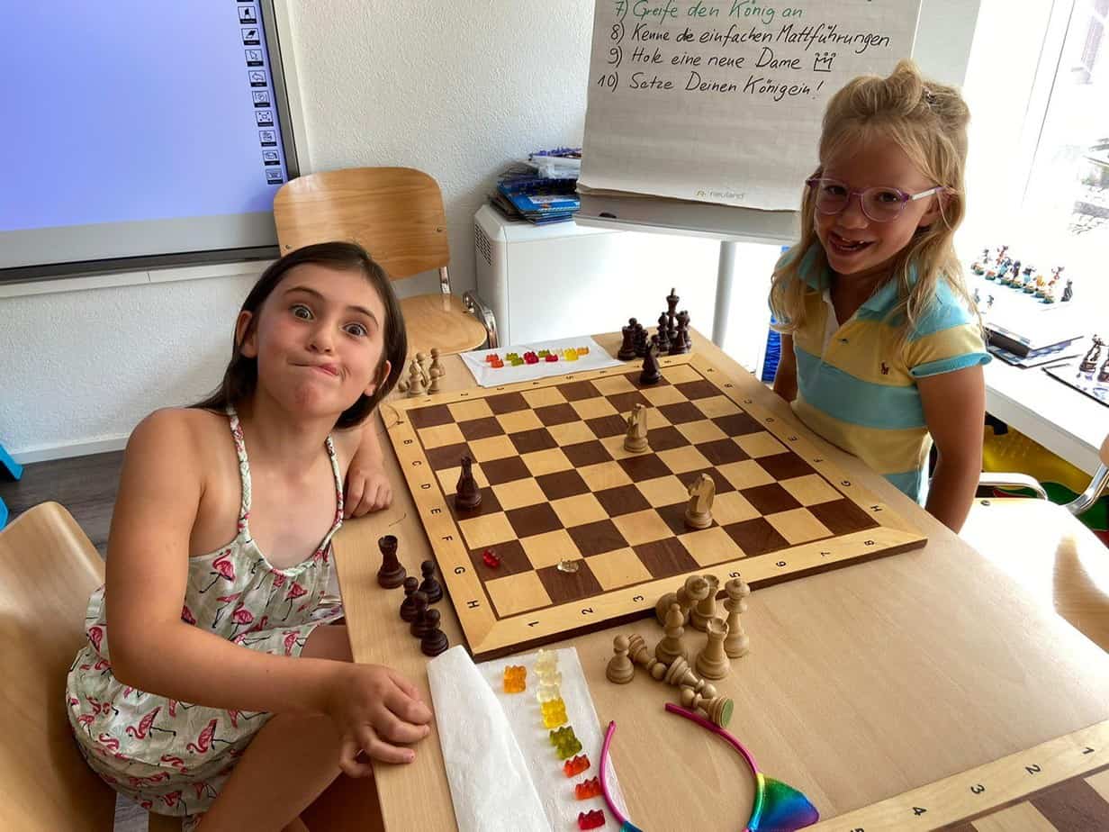2 Mädchen haben Spass bei einer Schachlektion mit Springern und Gummibärchen