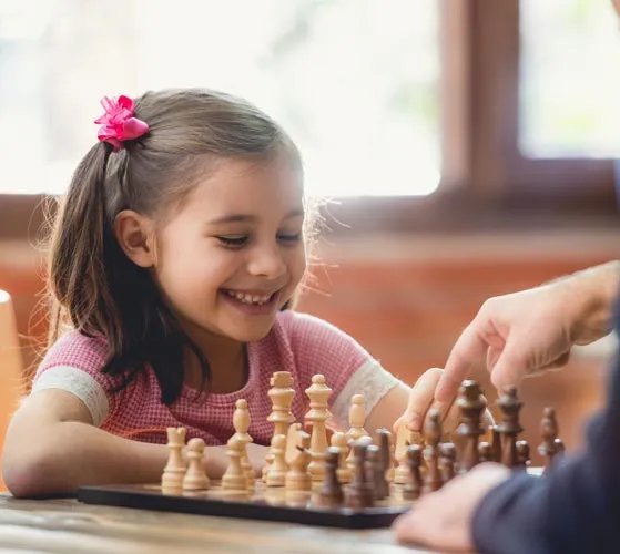 Happy girl receiving a chess lesson from a teacher